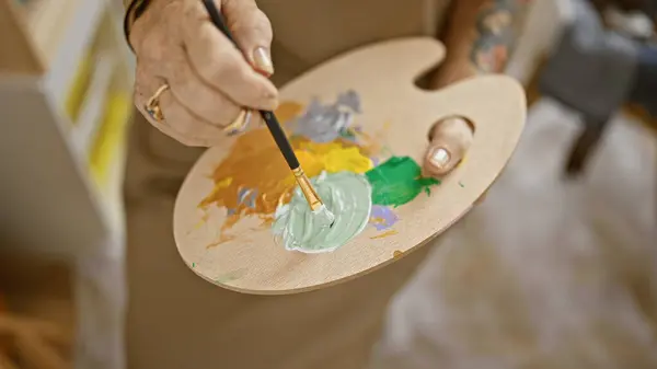 Senior woman artist\'s hands joyfully mix colors at art studio while mastering her painting hobby
