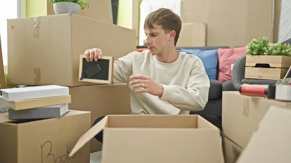 Young caucasian man packing cardboard box at new home