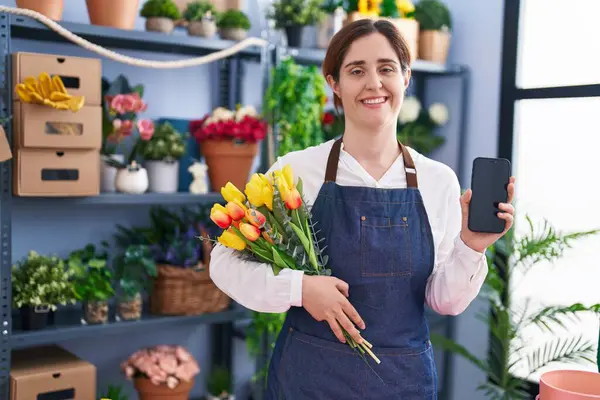 Brunette woman working at florist shop holding smartphone smiling with a happy and cool smile on face. showing teeth.