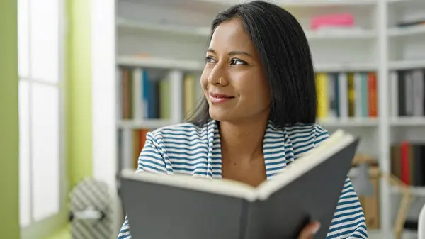 African american woman student reading book smiling at library university