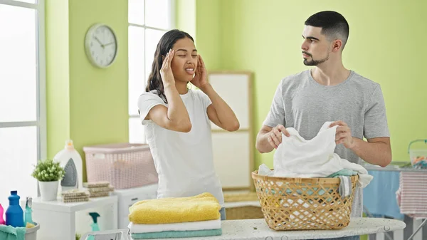 Exhausted love-struck couple suffering headache while tackling tedious laundry chores in their beautiful indoor laundry room