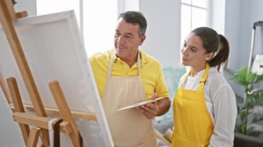 Gülümseyen erkek ve kadın sanatçılar bir sanat stüdyosunda neşeyle sarılıyorlar, birlikte çiziyorlar ve yaratıcılığı kucaklıyorlar.