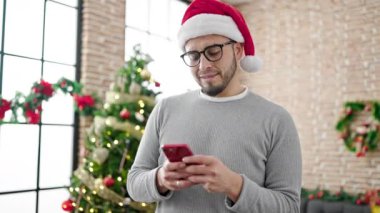 Noel Baba şapkalı adam yılbaşı ağacının yanında akıllı telefon kullanıyor. Noel kutlaması konsepti