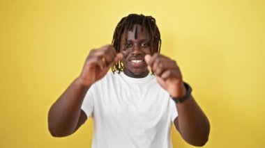 Afro-Amerikalı adam sarı arka planda başparmak gösteriyor.