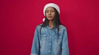 Kırmızı arka planda üzgün görünen, Noel Baba şapkalı genç melez kadın.