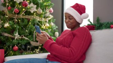 Noel Baba şapkalı kadın oturma odasında Noel ağacıyla Noel 'i kutluyor.