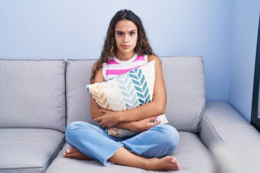 Evdeki koltukta oturan Latin kökenli genç kadın şüpheci ve gergin, sorun yüzünden surat asıyor. negatif kişi. 