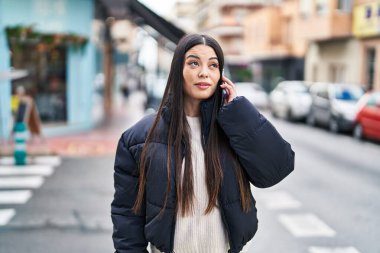 Young beautiful hispanic woman talking on smartphone with relaxed expression at street