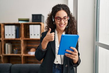 Dokunmatik kulaklık takan genç İspanyol kadın mutlu ve olumlu gülümsüyor, başparmağıyla mükemmel ve onay işareti yapıyor. 