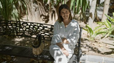 Parktaki bankta oturmuş gülümseyen güzel İspanyol kadın.