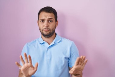 İspanyol adam pembe arka planda duruyor. Avuçlarını hareket ettiriyor. Korkmuş ve iğrenç bir ifadeyle reddediyor. Dur ve yasakla. 