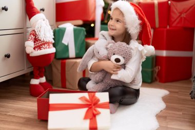 Sevimli İspanyol kız oyuncak ayıyı kucaklıyor. Evde Noel ağacının yanında oturuyor.