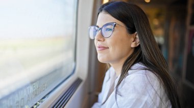 Genç, güzel İspanyol kadın mutlu bir şekilde gülümsüyor. Tren vagonunun içinden bakıyor.