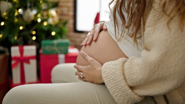 Karnına masaj yapan hamile bir kadın Noel 'i evde kutluyor.