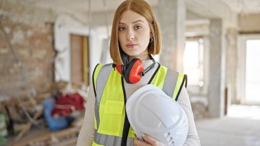 Sarışın genç bir mimar. İnşaat alanında kasketli gevşek bir ifadeyle duruyor.