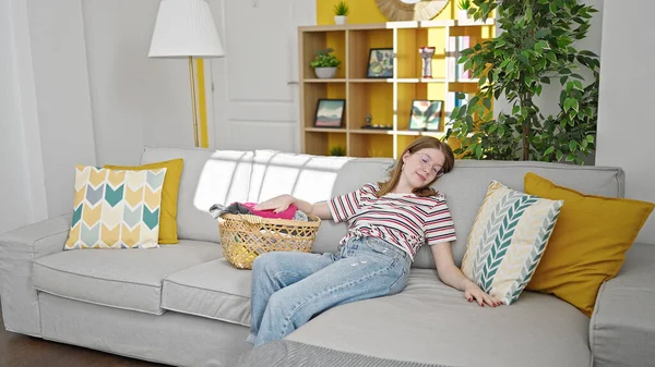 Young blonde woman falling on sofa tired for laundry at home
