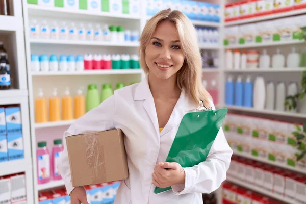 Young caucasian woman working at pharmacy drugstore holding box doing inventory smiling with a happy and cool smile on face. showing teeth.
