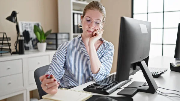 Young blonde woman business worker using computer and earphones taking notes at office