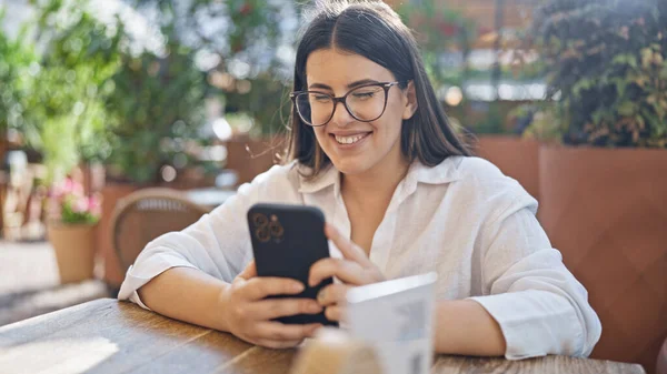 Young beautiful hispanic woman smiling happy using smartphone sitting on the table at bar terrace