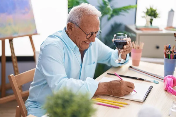 シニア白髪の男アーティストがノートに絵を描くアートスタジオでワインを飲む — ストック写真