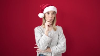 Kırmızı arka planda Noel Baba şapkalı düşünceli genç bayan.
