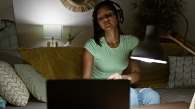 Evdeki kanepede rahatça müzik dinleyen genç Latin kadın.