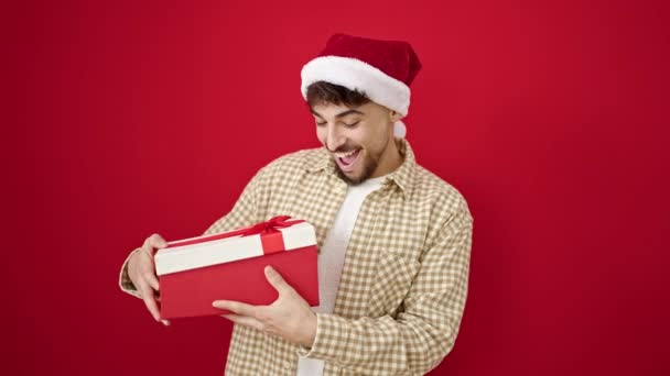 Молодой Араб Рождественской Шляпе Распаковывает Подарок Выглядя Расстроенным Изолированном Красном — стоковое видео