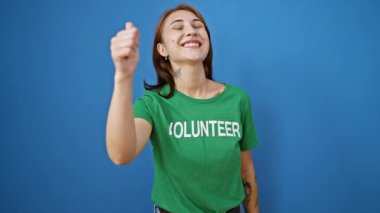 Genç bayan gönüllü gülümsüyor. Kendine güveniyor. Mavi arka planda el hareketi yapıyor.