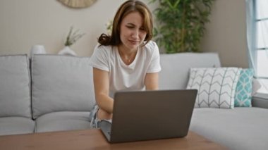 Dizüstü bilgisayar kullanan genç bir kadın eve üzgün üzgün bakıyor.