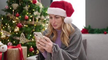 Genç ve güzel İspanyol kadın akıllı telefon kullanarak Noel 'i evde kutluyor.