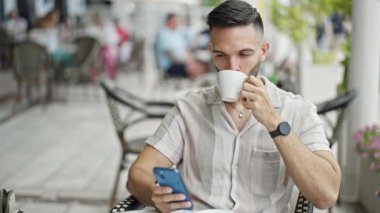 Genç İspanyol adam akıllı telefon kullanıyor. Kahve dükkanının terasında kahve içiyor.