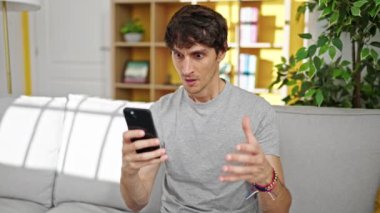 Genç İspanyol adam akıllı telefon ve kredi kartıyla alışveriş yapıyor. Evde üzgün görünüyor.