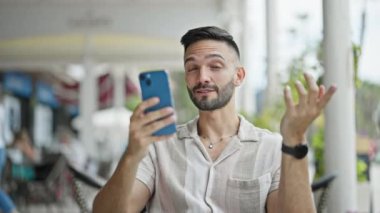 Latin asıllı genç adam gülümsüyor. Kahve dükkanının terasında kendine güveniyor.