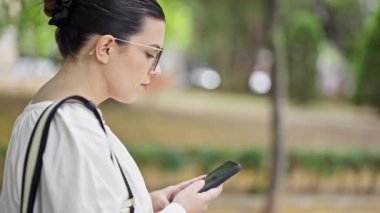 Parkta akıllı telefon kullanan genç ve güzel bir İspanyol kadın.