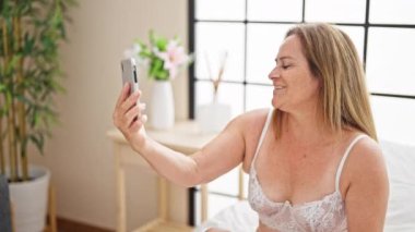 Orta yaşlı İspanyol kadın seksi iç çamaşırları giyiyor. Yatak odasında video görüşmesi yapıyor.