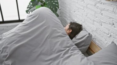 Güzel İspanyol bir kadın rahat pijamalarıyla rahatlıyor, kollarını rahatça açıyor, sabah yatak odasında uyanıyor.