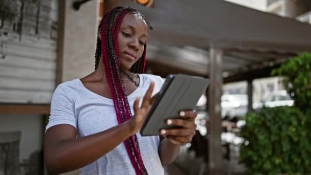自信的非洲裔美国女人 带着幸福的笑容 用她的触摸板在阳光灿烂的咖啡店露台上 展示着一种快乐而充满活力的生活方式 — 图库视频影像