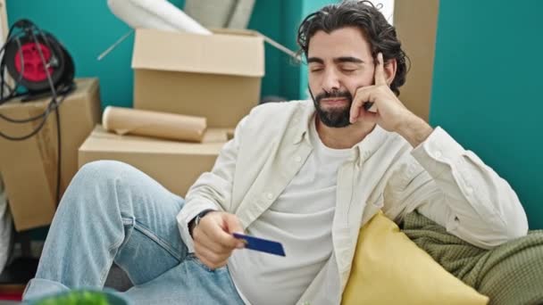 Jovem Hispânico Segurando Cartão Crédito Sentado Sofá Pensando Nova Casa — Vídeo de Stock