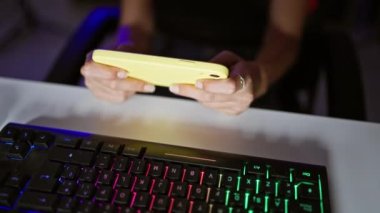 Oyunun pençesinde, İspanyol yetişkin kadın streamer 'ın elleri geceleyin karanlık oyun odasında akıllı telefonuyla video oyunu oynuyor.
