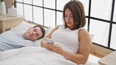 Erkek arkadaşı yatak odasında uyurken akıllı telefon kullanan güzel bir çift.