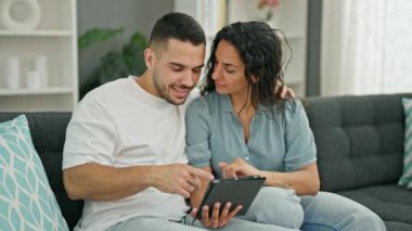 Man and woman couple using touchpad sitting on sofa at home