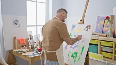 Yakışıklı genç sanatçı, rahat ama ciddi, önlüğünü çıkarıyor ve heyecan verici bir sanat stüdyosunda büyüleyici bir çizimi tamamlıyor.