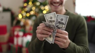 Genç İspanyol adam evdeki Noel ağacının yanındaki koltukta oturmuş dolar sayıyor.