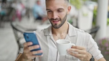 Genç İspanyol adam akıllı telefon kullanıyor. Kahve dükkanının terasında kahve içiyor.