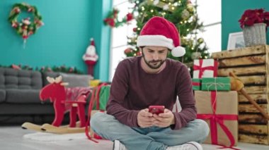Genç İspanyol adam akıllı telefon kullanarak Noel 'i kutluyor. Evde üzgün görünüyor.