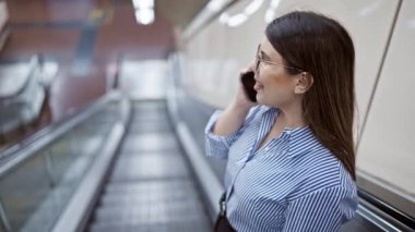 Madrid metro istasyonunda yürüyen merdivende duran genç ve güzel İspanyol kadın telefonda konuşuyor.