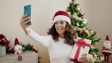 Orta yaşlı İspanyol kadın evde elinde Noel hediyesi ile video görüşmesi yapıyor.