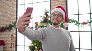 İspanyol adam evde Noel şapkası takıp selfie çekiyor.