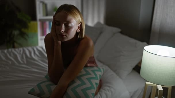 ベッドに座っている若い金髪の女性 寝室で子宮頸部の痛みのために苦しむ — ストック動画
