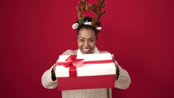 Afroamerikanerin Mit Weihnachtsgeschenk Trägt Rentierohren Über Isoliertem Rotem Hintergrund — Stockvideo